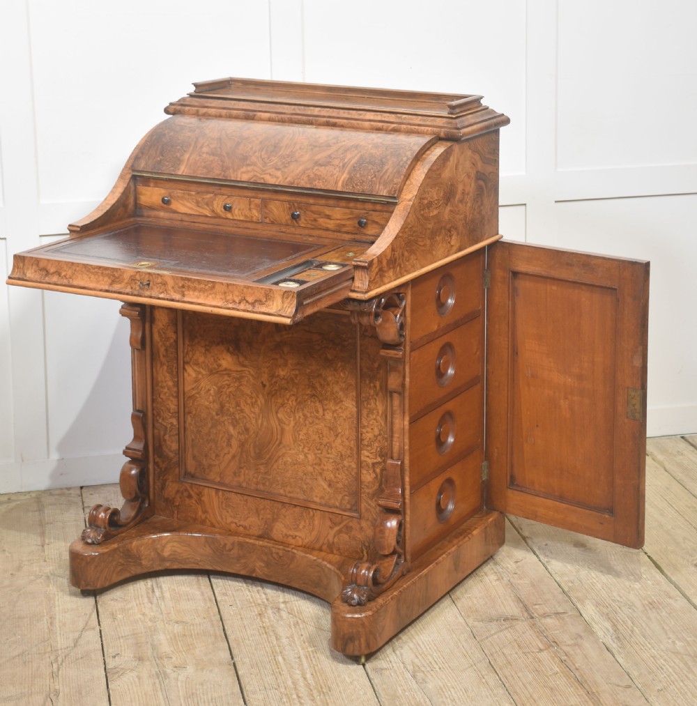 A Victorian burr walnut Davenport desk featuring a pop-up stationery cabinet decorated with floral marquetry, a sloped write top, and carved scroll supports. View VI