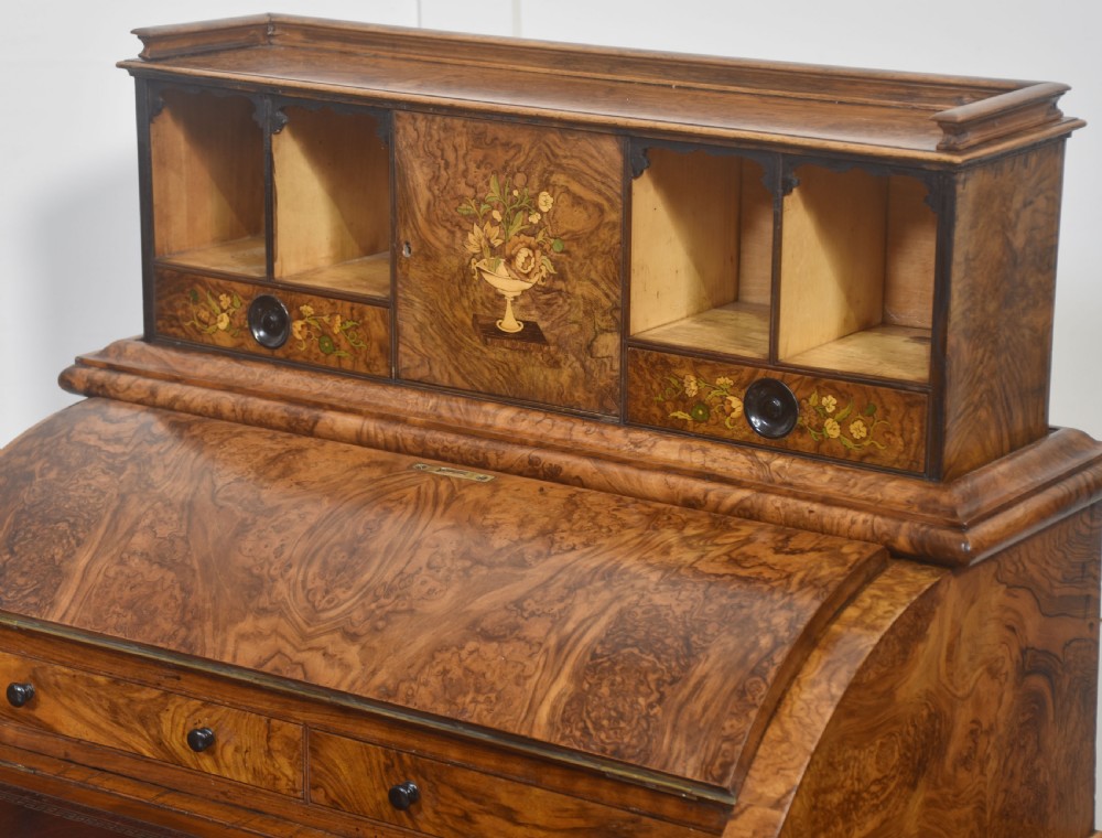 A Victorian burr walnut Davenport desk featuring a pop-up stationery cabinet decorated with floral marquetry, a sloped write top, and carved scroll supports. View IX