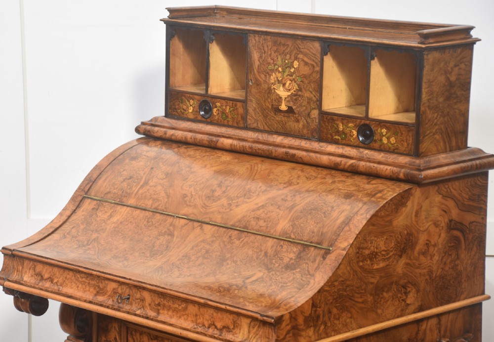 A Victorian burr walnut Davenport desk featuring a pop-up stationery cabinet decorated with floral marquetry, a sloped write top, and carved scroll supports. View XI
