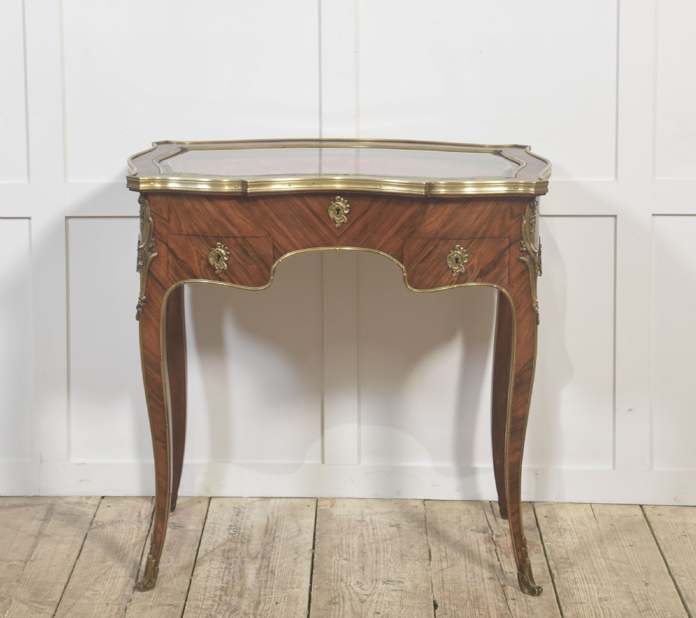 A French Louis XV style kingwood bijouterie table featuring a glazed display lid, curved aprons with gilt-bronze escutcheons, and slender cabriole legs with brass mounts.