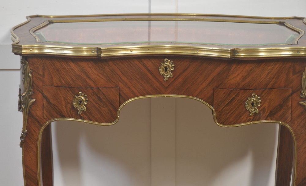 A French Louis XV style kingwood bijouterie table featuring a glazed display lid, curved aprons with gilt-bronze escutcheons, and slender cabriole legs with brass mounts. View II