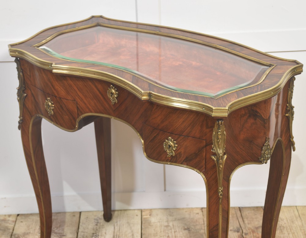 A French Louis XV style kingwood bijouterie table featuring a glazed display lid, curved aprons with gilt-bronze escutcheons, and slender cabriole legs with brass mounts. View V