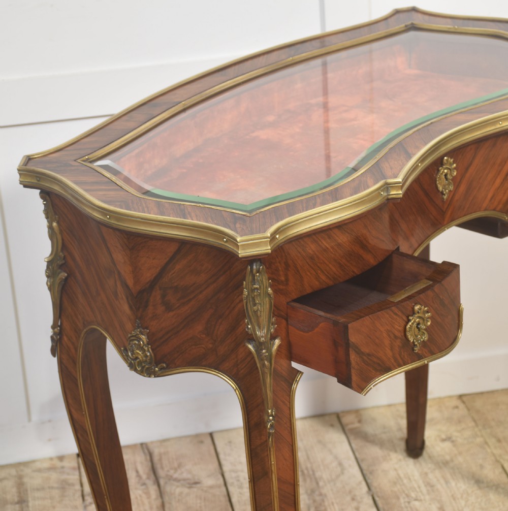 A French Louis XV style kingwood bijouterie table featuring a glazed display lid, curved aprons with gilt-bronze escutcheons, and slender cabriole legs with brass mounts. View IX