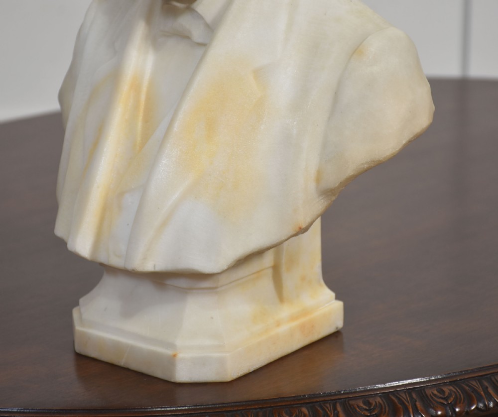 A carved cream and off-white marble portrait bust of a bearded gentleman wearing a suit jacket, waistcoat, and bow tie on a integral base. View VII