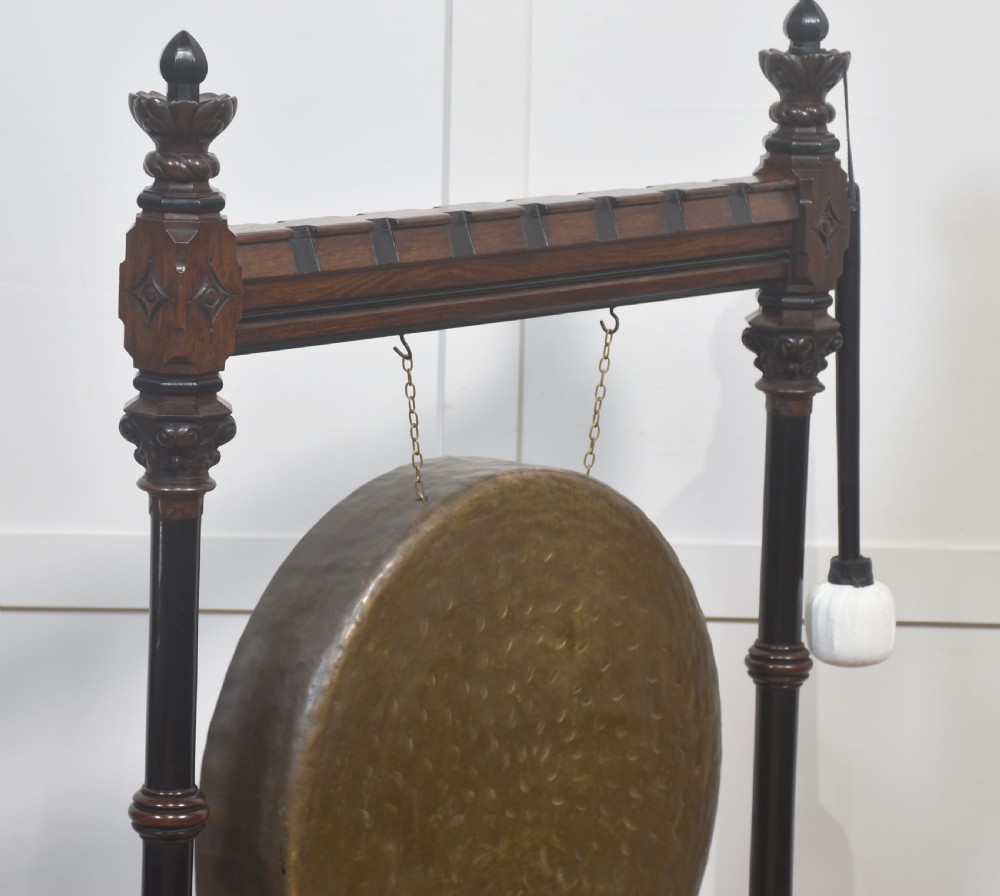 A floor-standing carved dark walnut frame with Gothic Revival motifs holding a large suspended circular brass gong and striker. View V