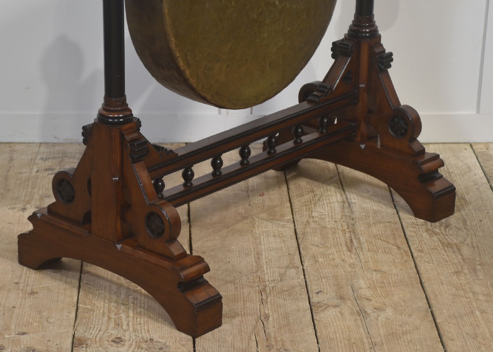 A floor-standing carved dark walnut frame with Gothic Revival motifs holding a large suspended circular brass gong and striker. View VII