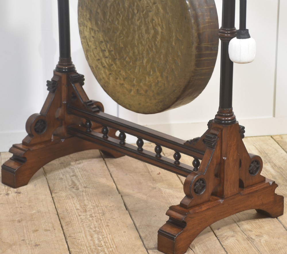 A floor-standing carved dark walnut frame with Gothic Revival motifs holding a large suspended circular brass gong and striker. View X