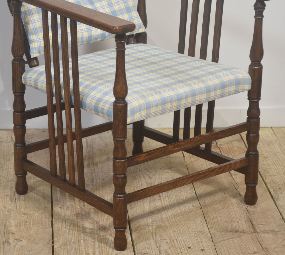 A dark oak reclining armchair featuring turned posts, vertical side slats, and a blue and yellow plaid upholstered cushion. View V