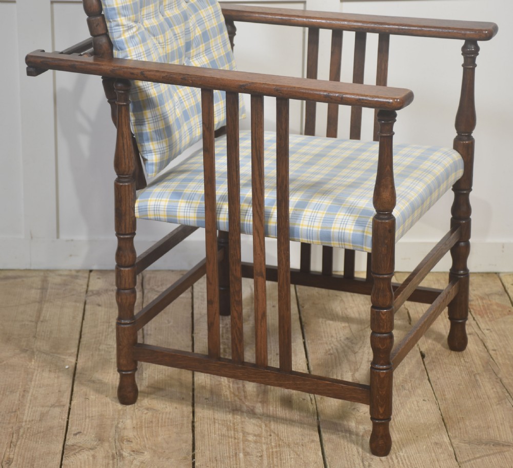 A dark oak reclining armchair featuring turned posts, vertical side slats, and a blue and yellow plaid upholstered cushion. View VIII