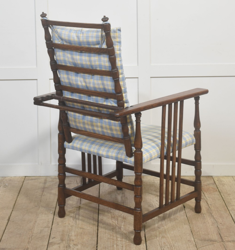 A dark oak reclining armchair featuring turned posts, vertical side slats, and a blue and yellow plaid upholstered cushion. View IX