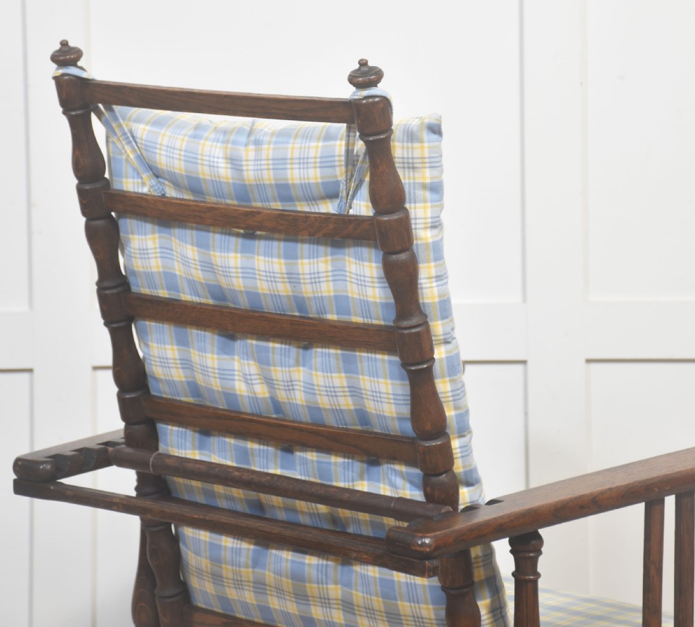 A dark oak reclining armchair featuring turned posts, vertical side slats, and a blue and yellow plaid upholstered cushion. View X