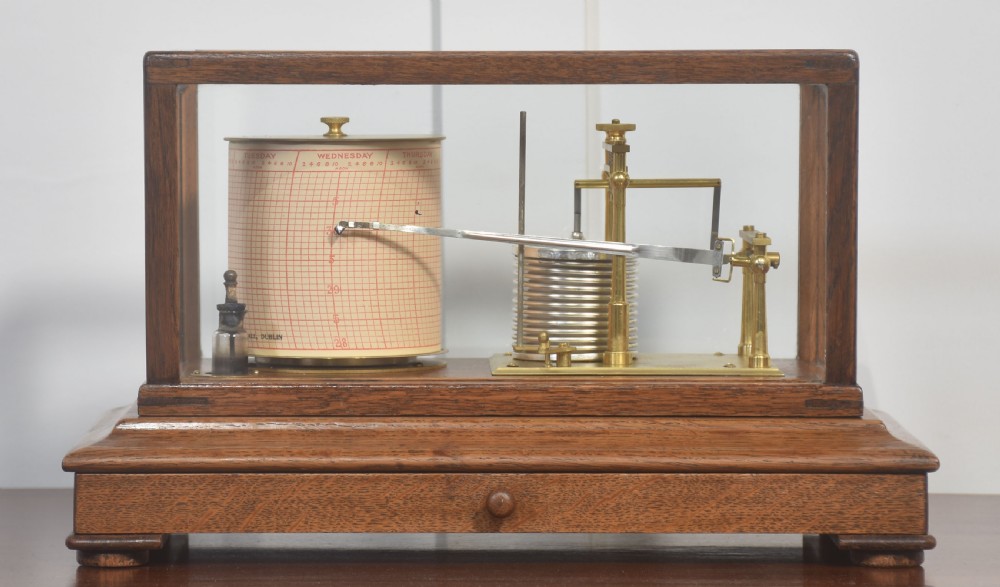 An antique barograph with a brass mechanism and paper chart drum enclosed within a glazed oak case with a bottom drawer.