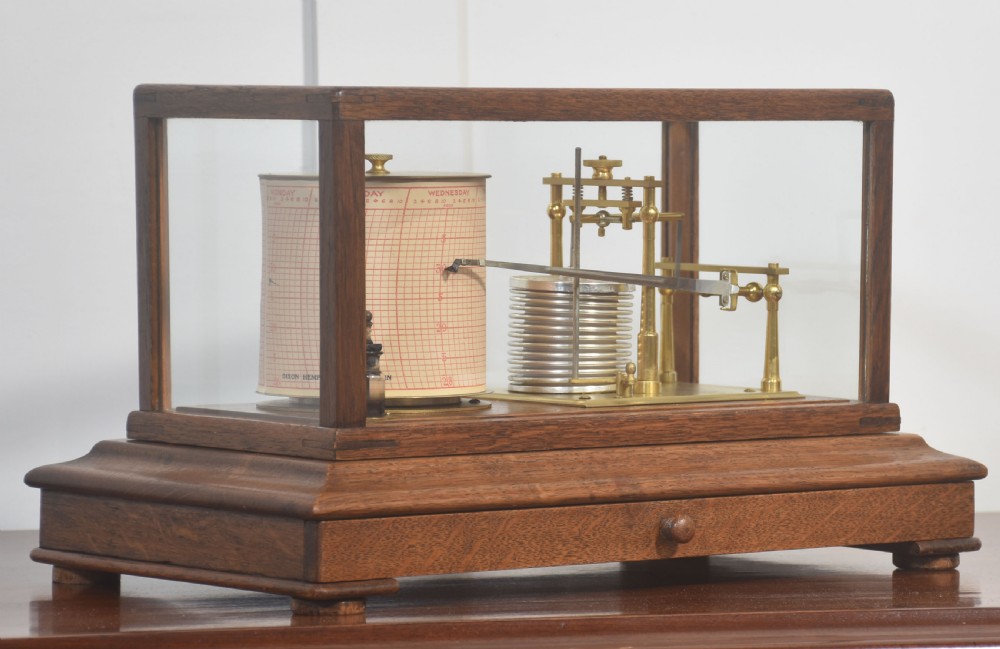 An antique barograph with a brass mechanism and paper chart drum enclosed within a glazed oak case with a bottom drawer. View II