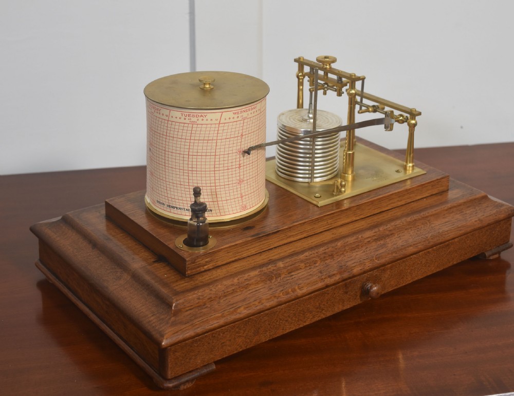 An antique barograph with a brass mechanism and paper chart drum enclosed within a glazed oak case with a bottom drawer. View IV