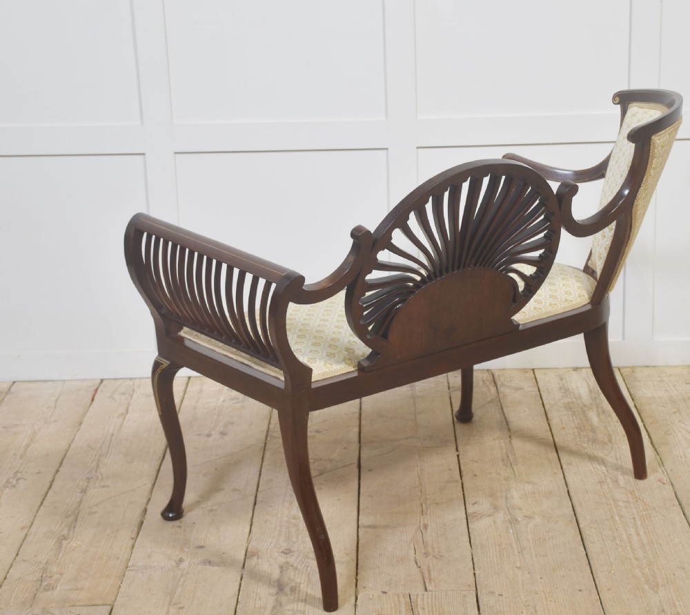 An antique mahogany settee featuring an openwork fan back with floral marquetry inlay, slatted side rails, and a cream pattern upholstered seat. View IX