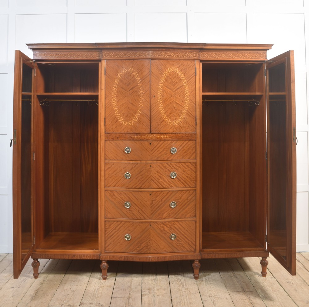 A large Edwardian inlaid satinwood compactum wardrobe featuring a central section with cupboard doors above four drawers, flanked by two full-length side doors. View IV