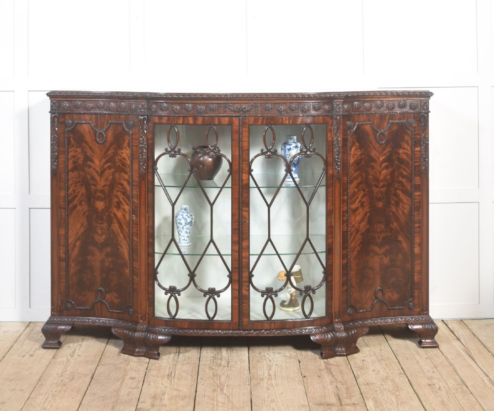 A wide mahogany display cabinet featuring flame mahogany veneered side doors, central astragal glazed double doors, carved rosettes along the frieze, and cabriole feet. View II