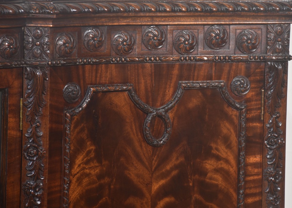 A wide mahogany display cabinet featuring flame mahogany veneered side doors, central astragal glazed double doors, carved rosettes along the frieze, and cabriole feet. View III