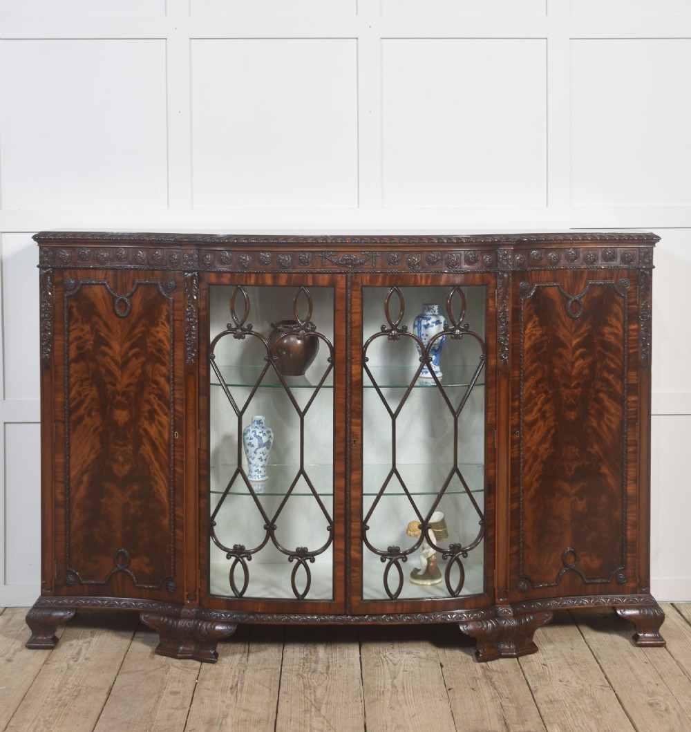 A wide mahogany display cabinet featuring flame mahogany veneered side doors, central astragal glazed double doors, carved rosettes along the frieze, and cabriole feet. View VI