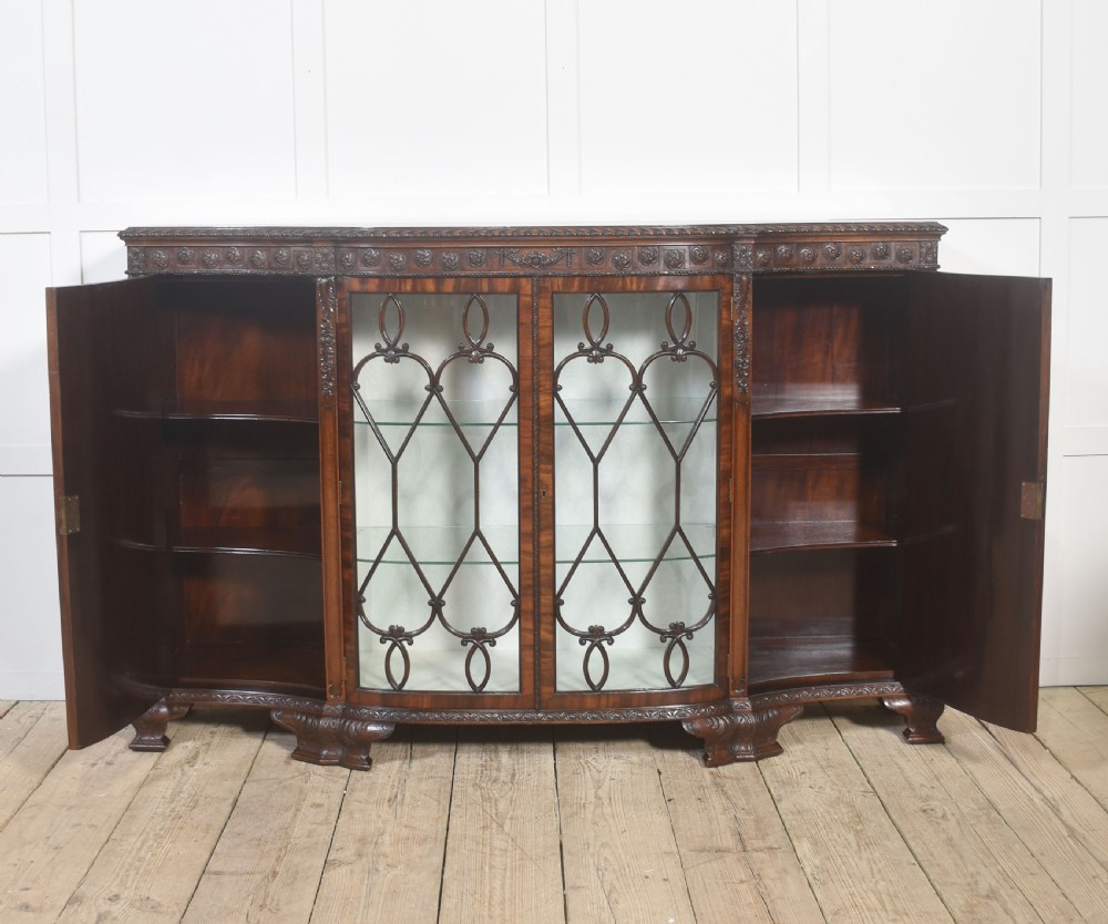 A wide mahogany display cabinet featuring flame mahogany veneered side doors, central astragal glazed double doors, carved rosettes along the frieze, and cabriole feet. View IX