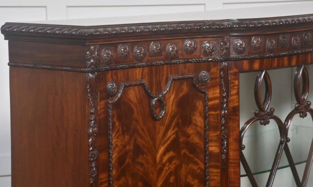 A wide mahogany display cabinet featuring flame mahogany veneered side doors, central astragal glazed double doors, carved rosettes along the frieze, and cabriole feet. View XII