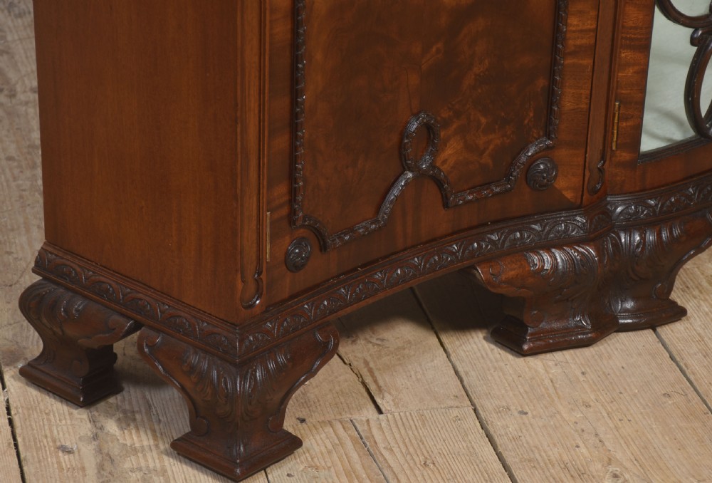 A wide mahogany display cabinet featuring flame mahogany veneered side doors, central astragal glazed double doors, carved rosettes along the frieze, and cabriole feet. View XIII