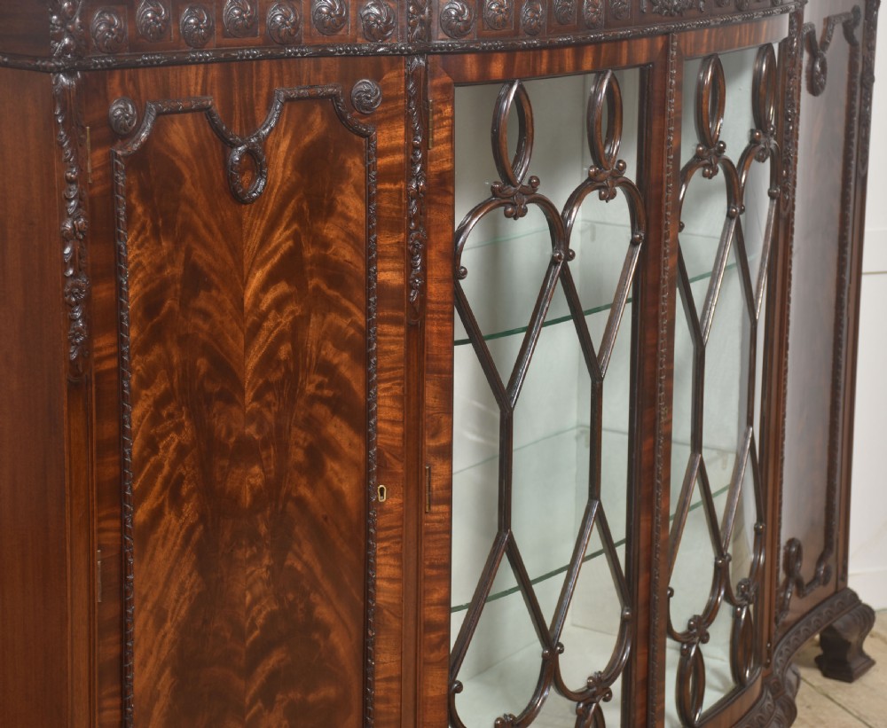 A wide mahogany display cabinet featuring flame mahogany veneered side doors, central astragal glazed double doors, carved rosettes along the frieze, and cabriole feet. View XIV