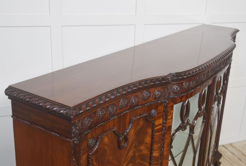 A wide mahogany display cabinet featuring flame mahogany veneered side doors, central astragal glazed double doors, carved rosettes along the frieze, and cabriole feet. View XV
