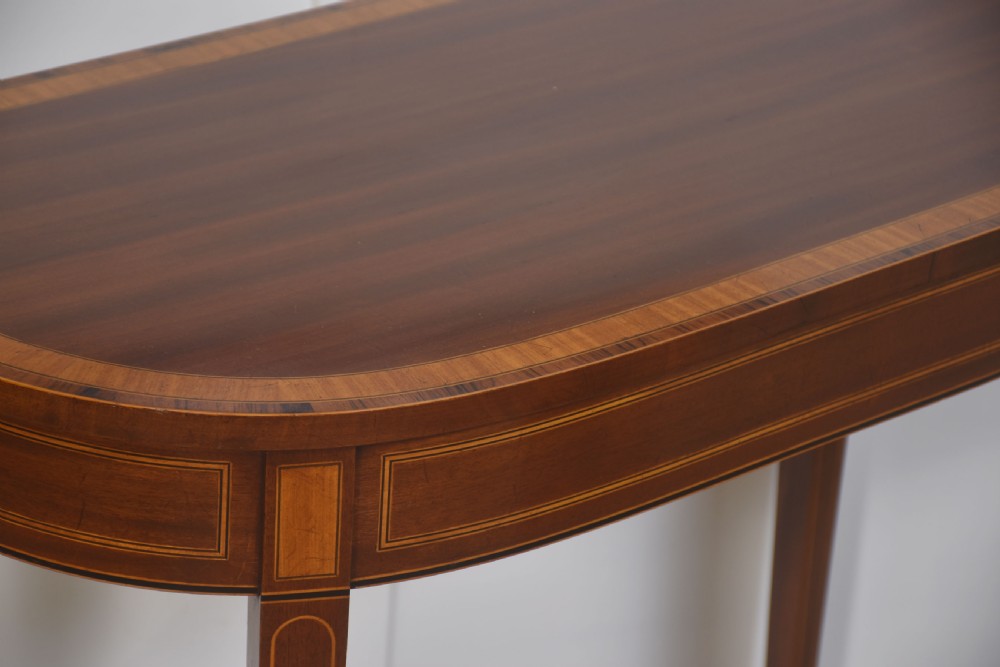 A demilune inlaid mahogany console table with square tapered legs shown beneath a matching rectangular crossbanded mahogany wall mirror. View VII