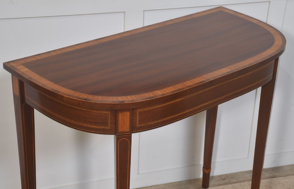 A demilune inlaid mahogany console table with square tapered legs shown beneath a matching rectangular crossbanded mahogany wall mirror. View VIII