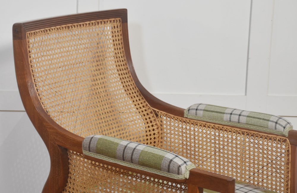 A mahogany bergere armchair featuring woven cane side and back panels, turned front legs on castors, and green plaid cushion upholstery. View VI