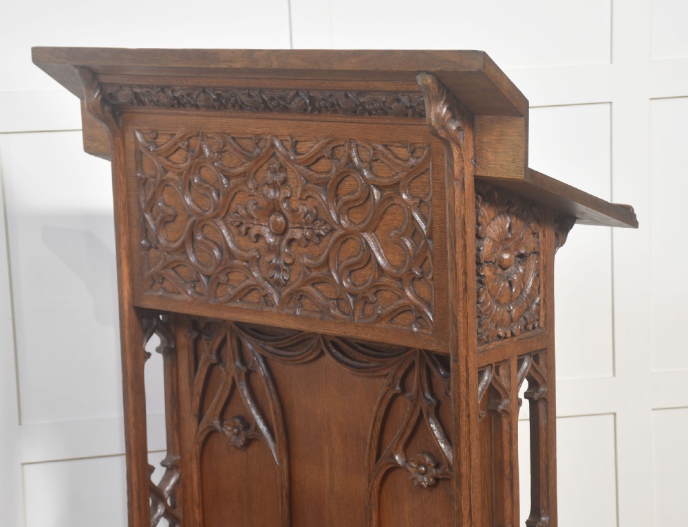 A floor-standing oak Gothic Revival lectern featuring carved blind tracery, floral rosettes, and a sloped top reading surface. View V