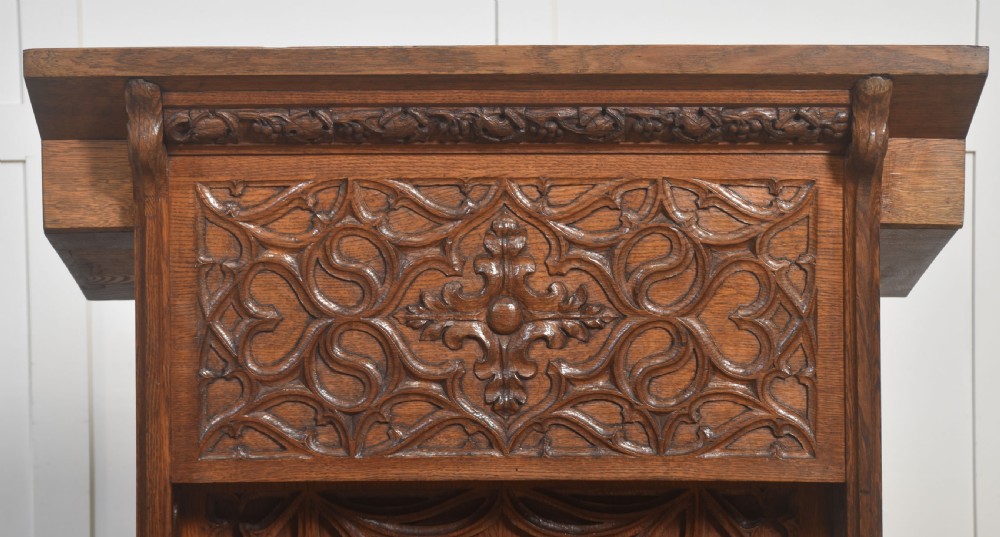 A floor-standing oak Gothic Revival lectern featuring carved blind tracery, floral rosettes, and a sloped top reading surface. View VII