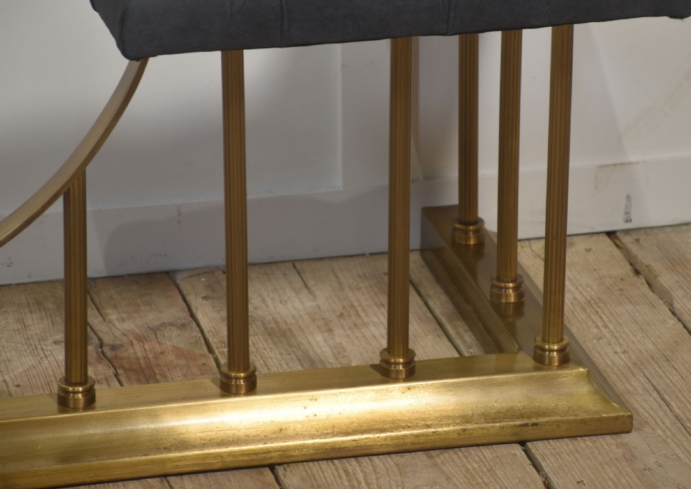 A solid brass club fender featuring twin button-upholstered grey corner seats supported by vertical brass spindles and a dipped central railing. View IV