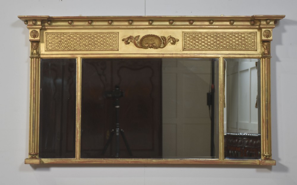 A large rectangular Neoclassical giltwood overmantel mirror featuring a three-plate glass design, frieze with spherule moulding and central shell motif, flanked by fluted side columns.