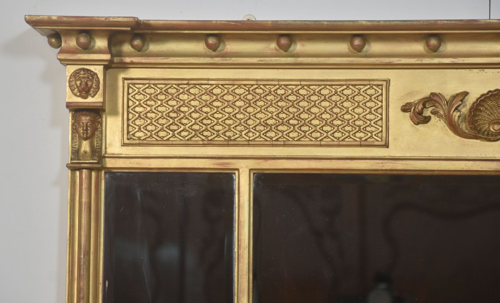 A large rectangular Neoclassical giltwood overmantel mirror featuring a three-plate glass design, frieze with spherule moulding and central shell motif, flanked by fluted side columns. View II