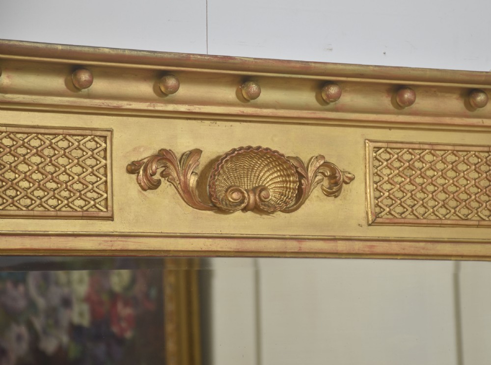 A large rectangular Neoclassical giltwood overmantel mirror featuring a three-plate glass design, frieze with spherule moulding and central shell motif, flanked by fluted side columns. View V