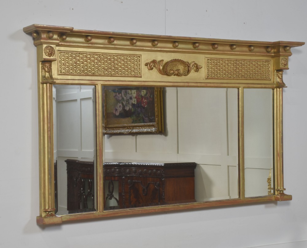 A large rectangular Neoclassical giltwood overmantel mirror featuring a three-plate glass design, frieze with spherule moulding and central shell motif, flanked by fluted side columns. View VI