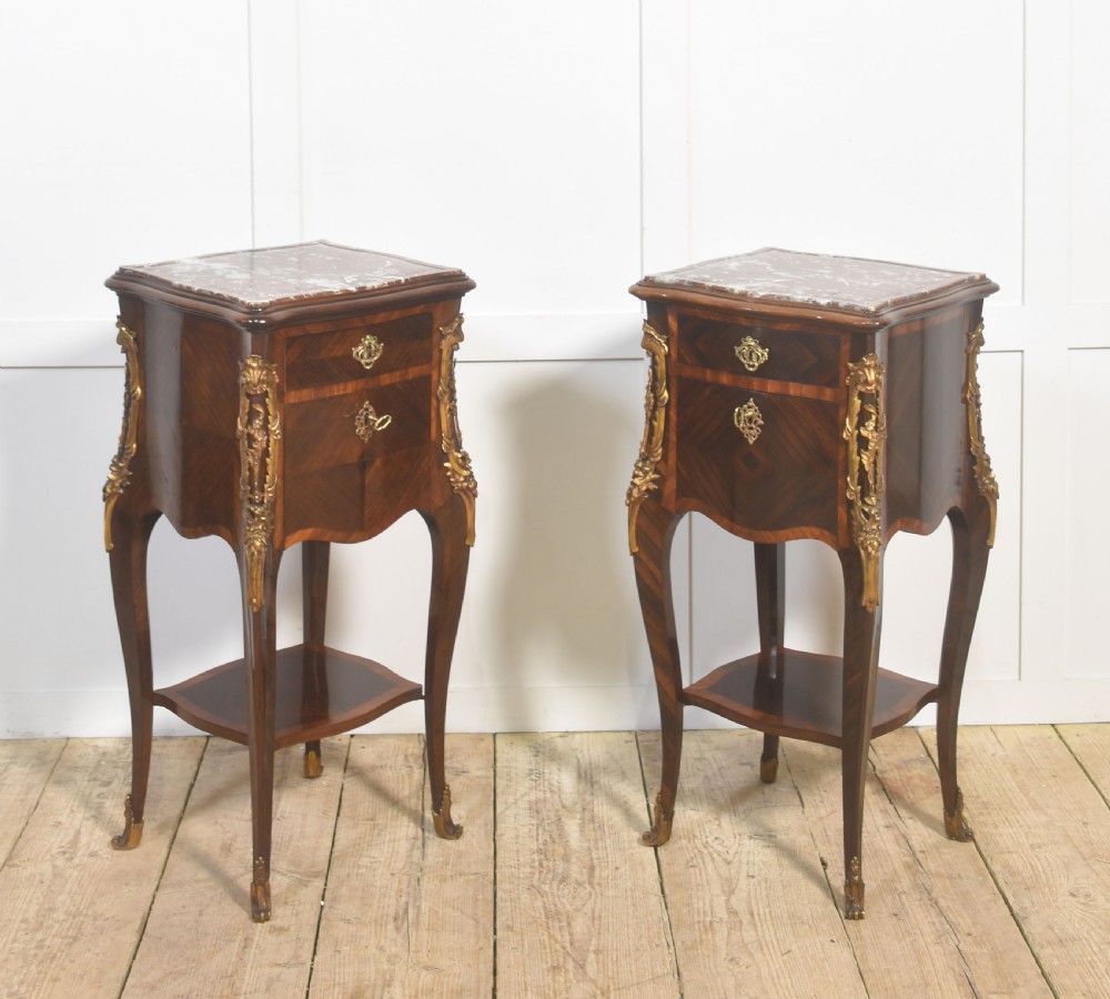 A pair of French Louis XV style bedside cabinets crafted with kingwood parquetry, dark marble tops, cabriole legs, and bronze mounts.
