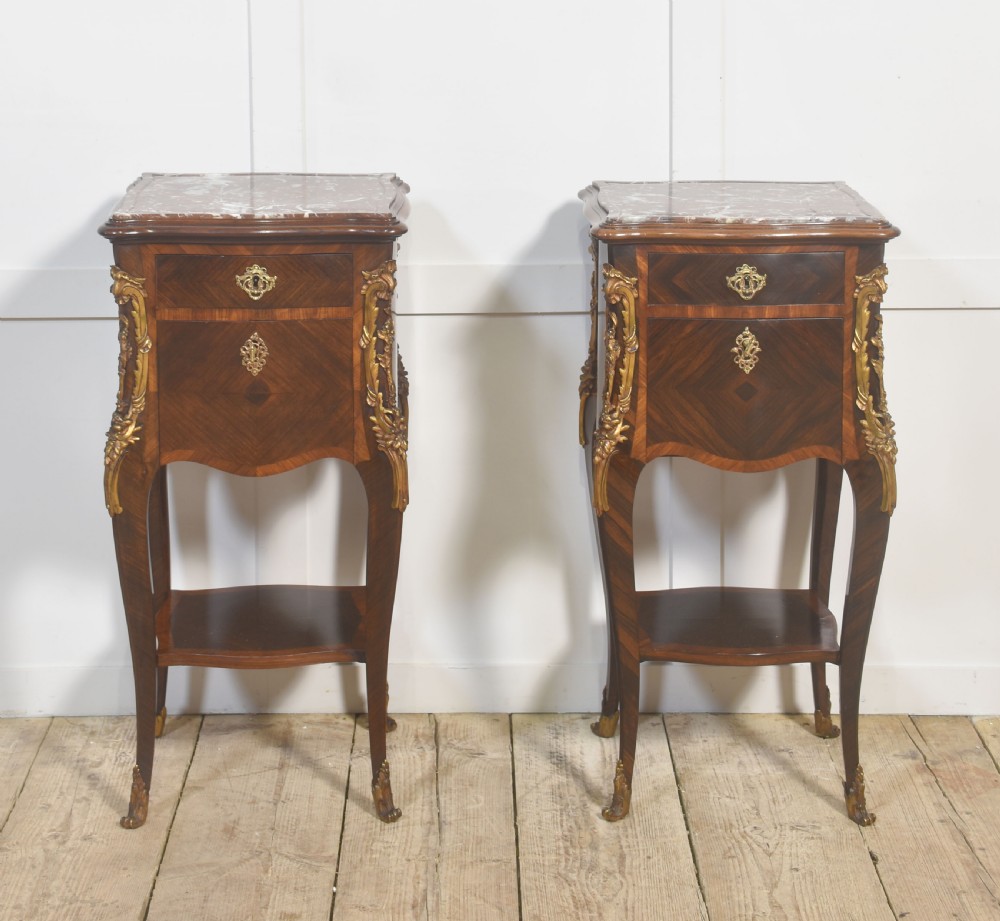 A pair of French Louis XV style bedside cabinets crafted with kingwood parquetry, dark marble tops, cabriole legs, and bronze mounts. View X