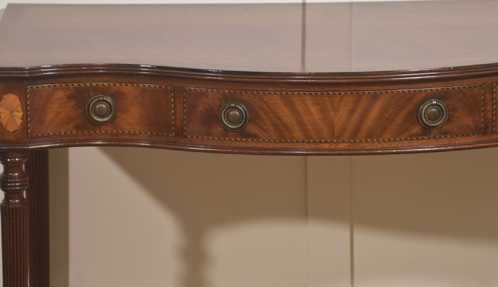 An inlaid mahogany writing table featuring a serpentine front, drawers with brass ring handles, oval patera marquetry, and fluted legs. View III