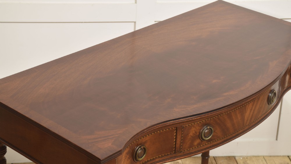 An inlaid mahogany writing table featuring a serpentine front, drawers with brass ring handles, oval patera marquetry, and fluted legs. View VIII