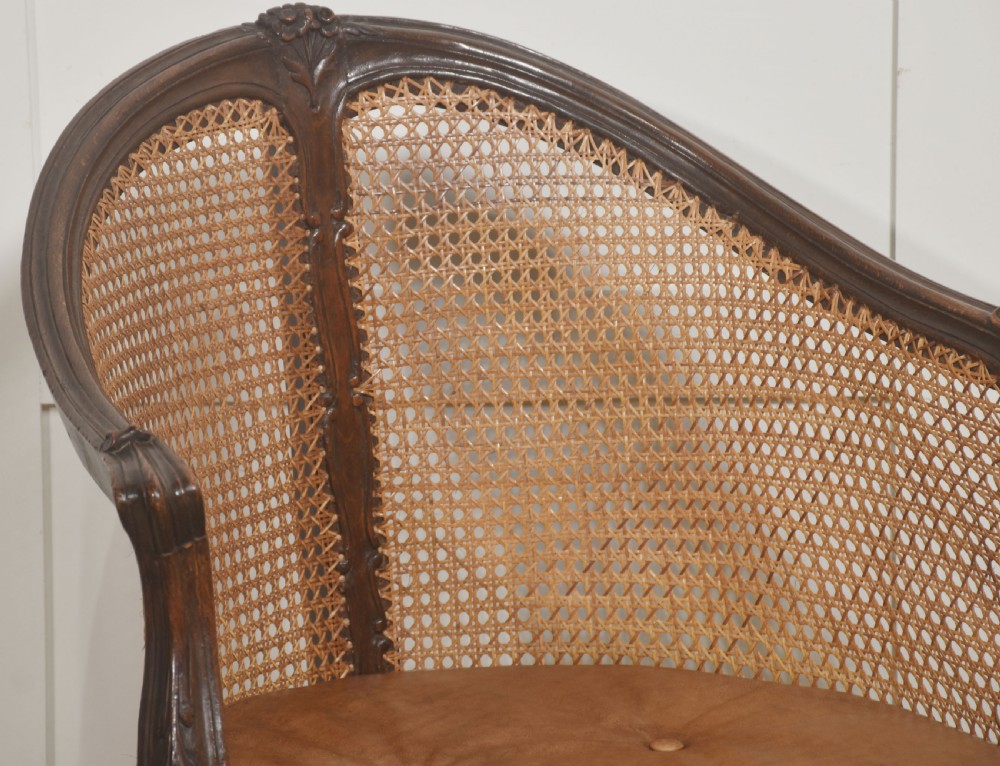 A French carved oak armchair featuring a curved woven cane backrest, a buttoned brown leather seat cushion, and carved cabriole legs. View IV