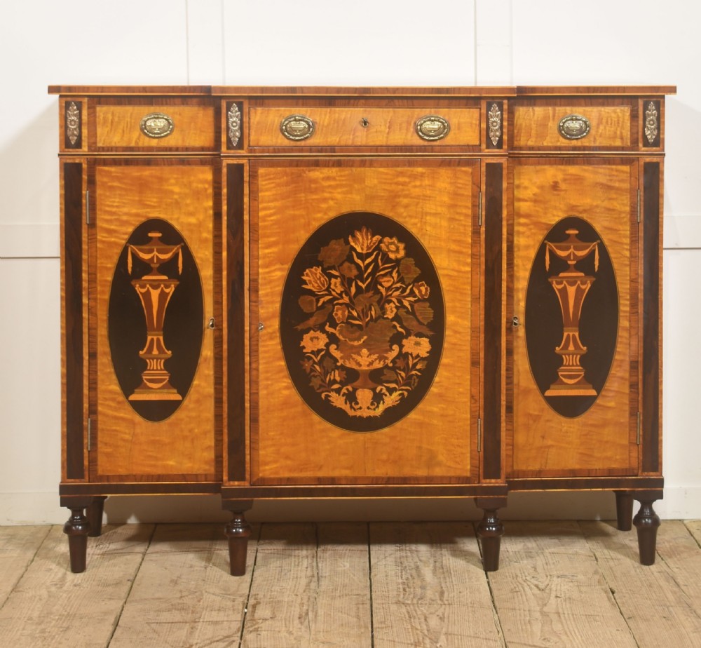 A Sheraton Revival satinwood sideboard with three upper drawers and three cupboard doors featuring oval marquetry panels of flowers and urns.