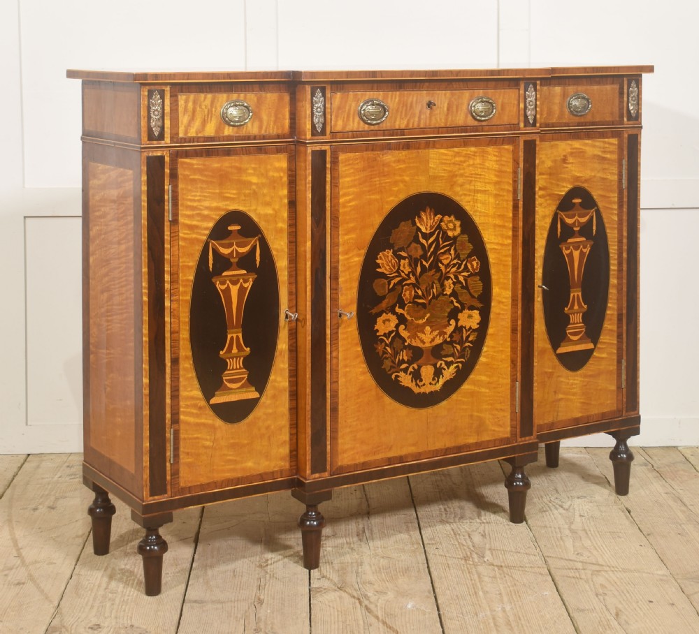 A Sheraton Revival satinwood sideboard with three upper drawers and three cupboard doors featuring oval marquetry panels of flowers and urns. View II