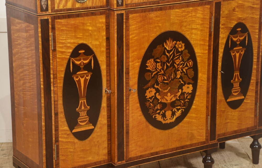 A Sheraton Revival satinwood sideboard with three upper drawers and three cupboard doors featuring oval marquetry panels of flowers and urns. View IV