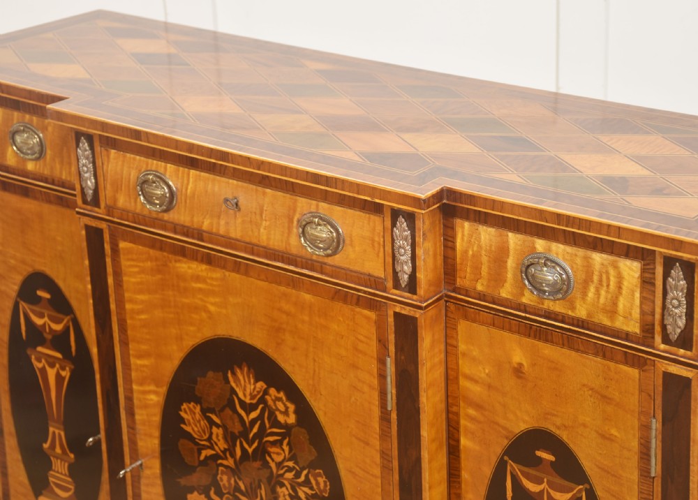 A Sheraton Revival satinwood sideboard with three upper drawers and three cupboard doors featuring oval marquetry panels of flowers and urns. View V