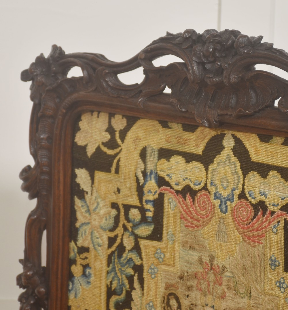 An ornate dark carved oak fire screen featuring a central needlepoint tapestry panel depicting a figure framed by elaborate scrollwork. View IV