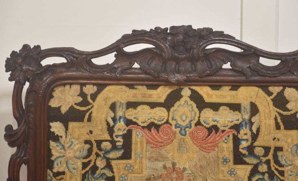 An ornate dark carved oak fire screen featuring a central needlepoint tapestry panel depicting a figure framed by elaborate scrollwork. View VII