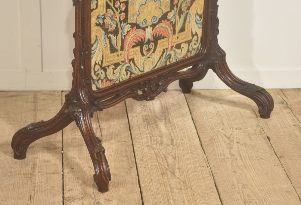 An ornate dark carved oak fire screen featuring a central needlepoint tapestry panel depicting a figure framed by elaborate scrollwork. View IX